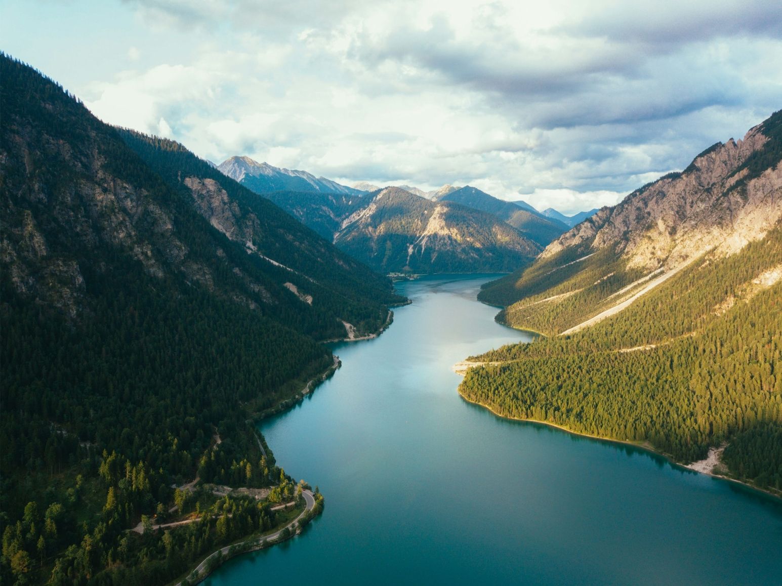 Fluss fließt durch bewaldete Berge unter bewölktem Himmel in einer alpinen Landschaft